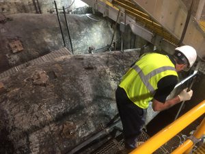 Technician in safety gear inspecting and maintaining heavy-duty machinery in an industrial environment.